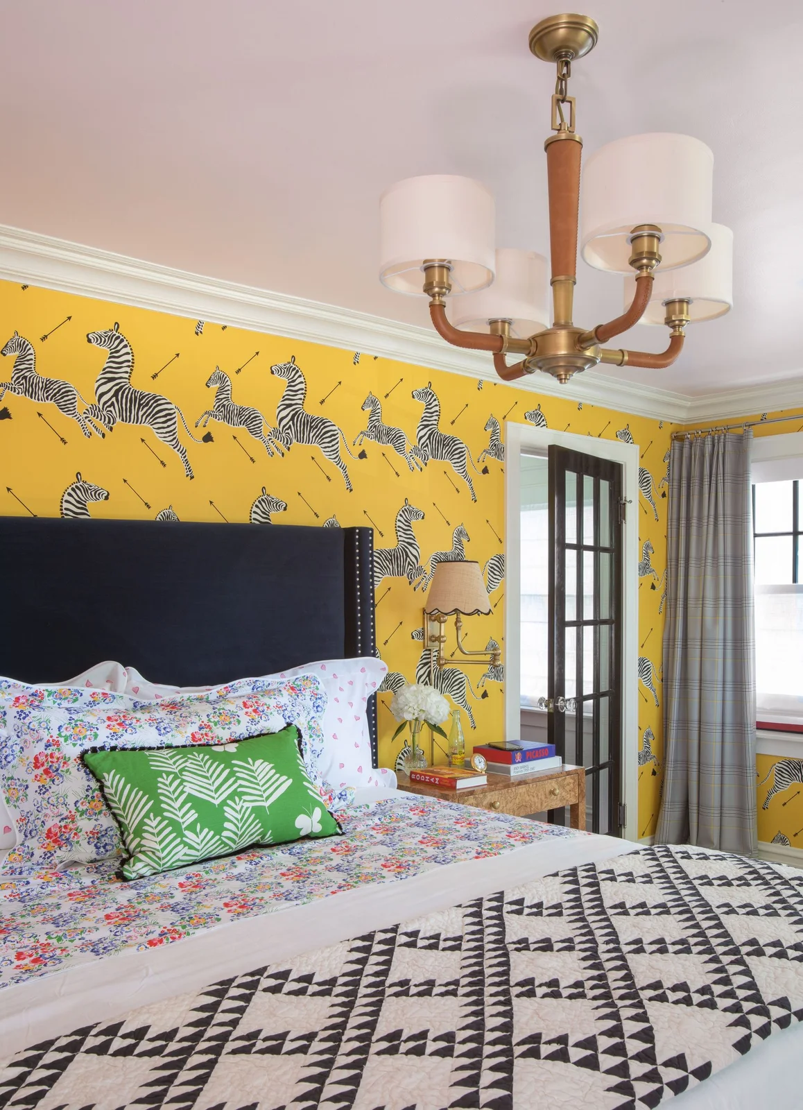 Yellow zebra-patterned wallpaper sits behind a tall navy headboard with floral white bedding, a green cushion and a geometric dark throw.