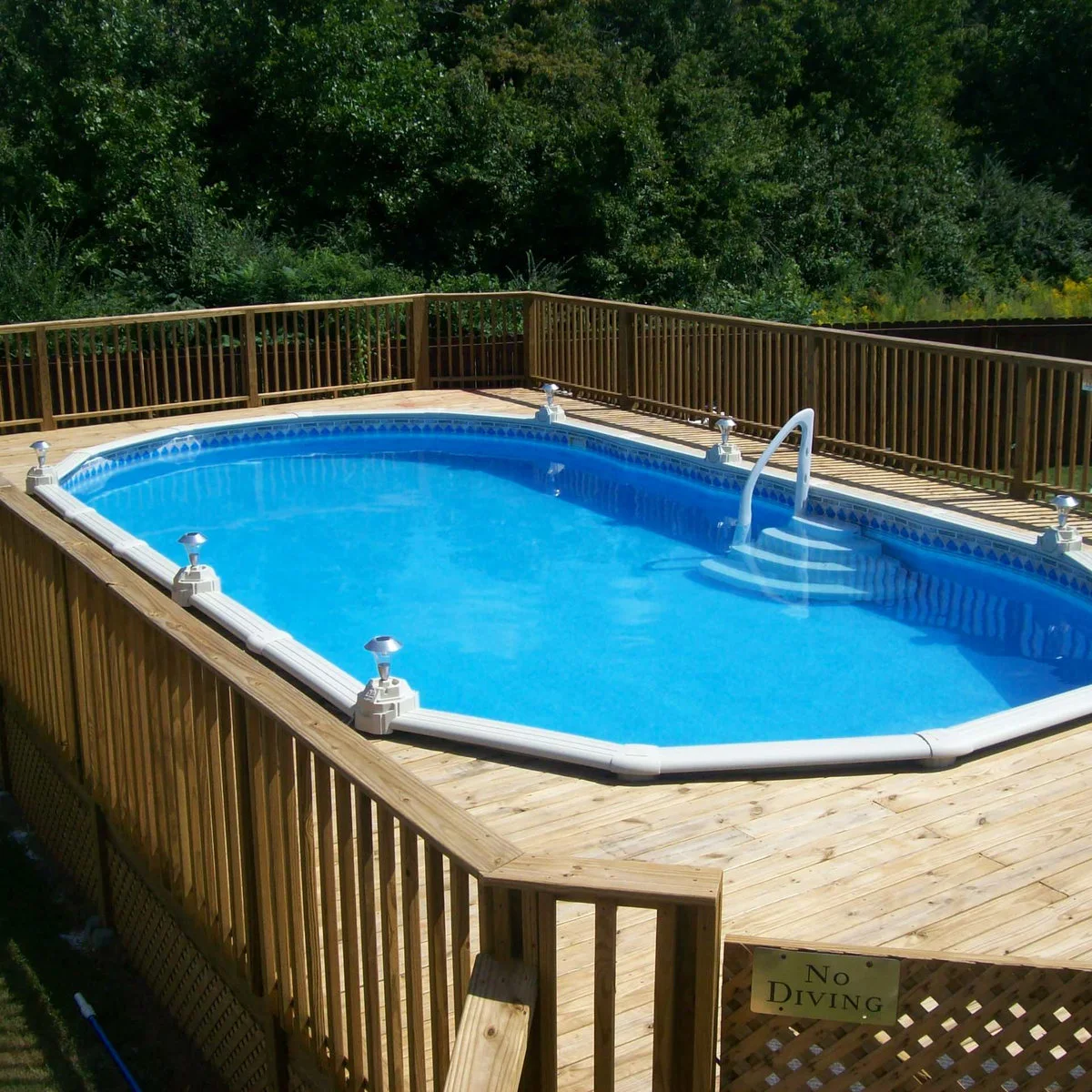 Oval above-ground pool inside a largely clear wood deck with perimeter rails, small post lights and white entry steps.