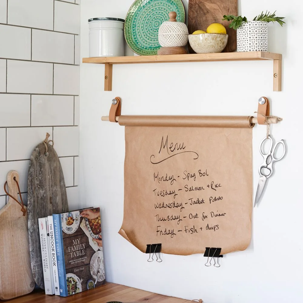 Brown paper roll suspended from tan wall loops below a kitchen shelf, with a handwritten menu
