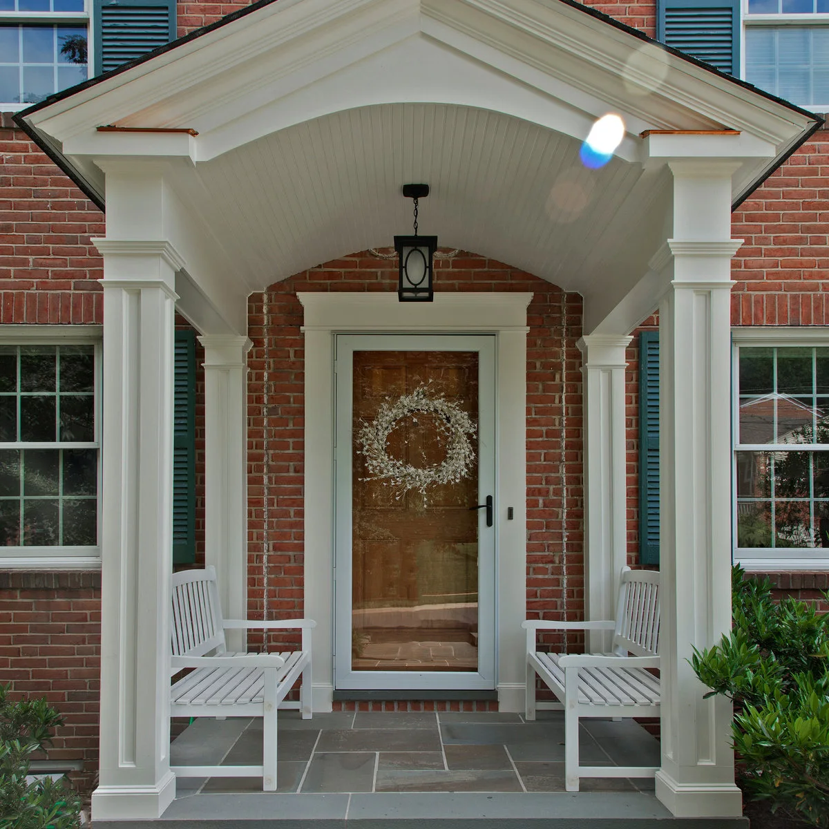 Small white portico with two short slatted benches beside a wood-colored front door