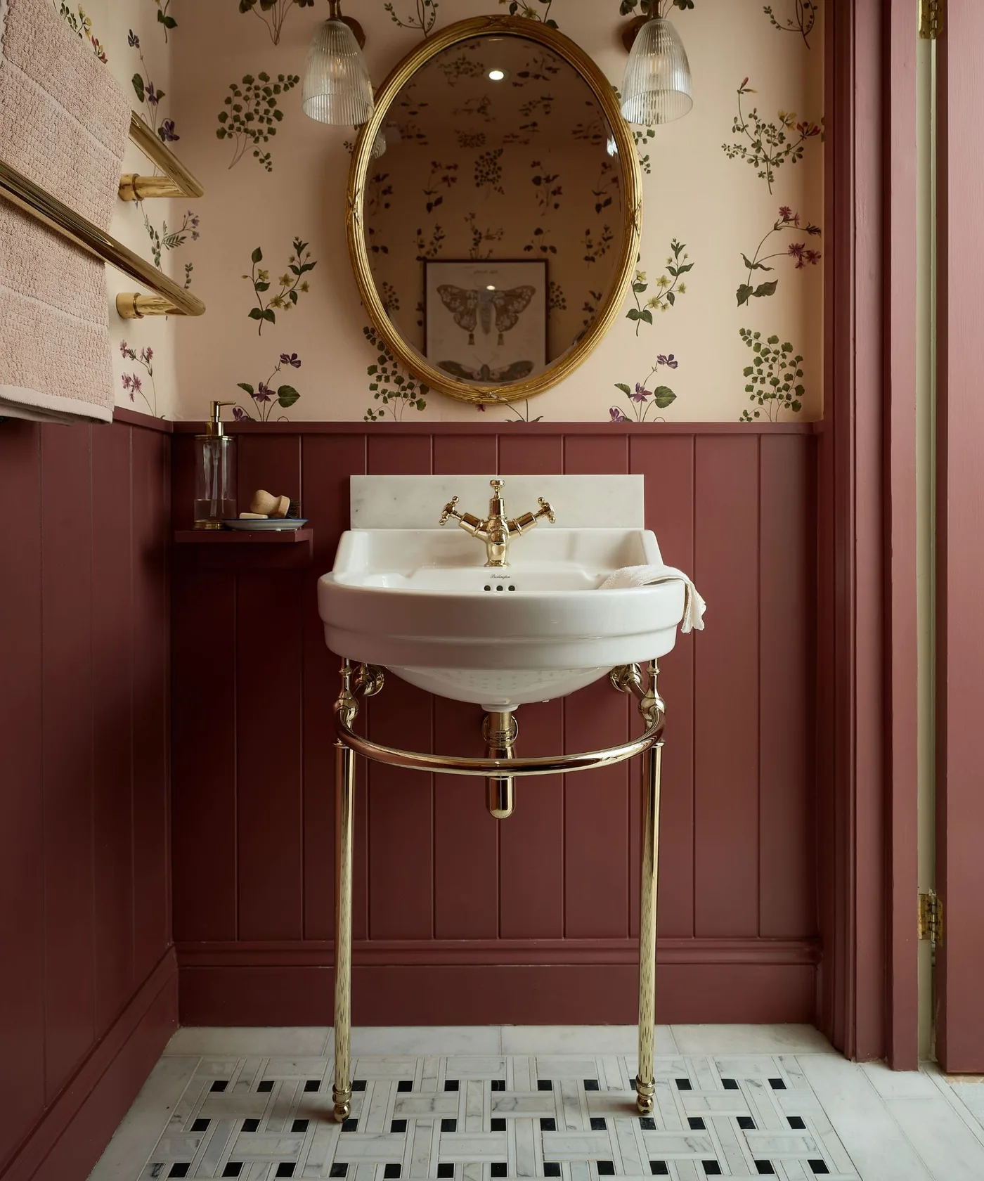 Red paneled powder room with floral wallpaper, oval mirror and white basin on warm-toned legs