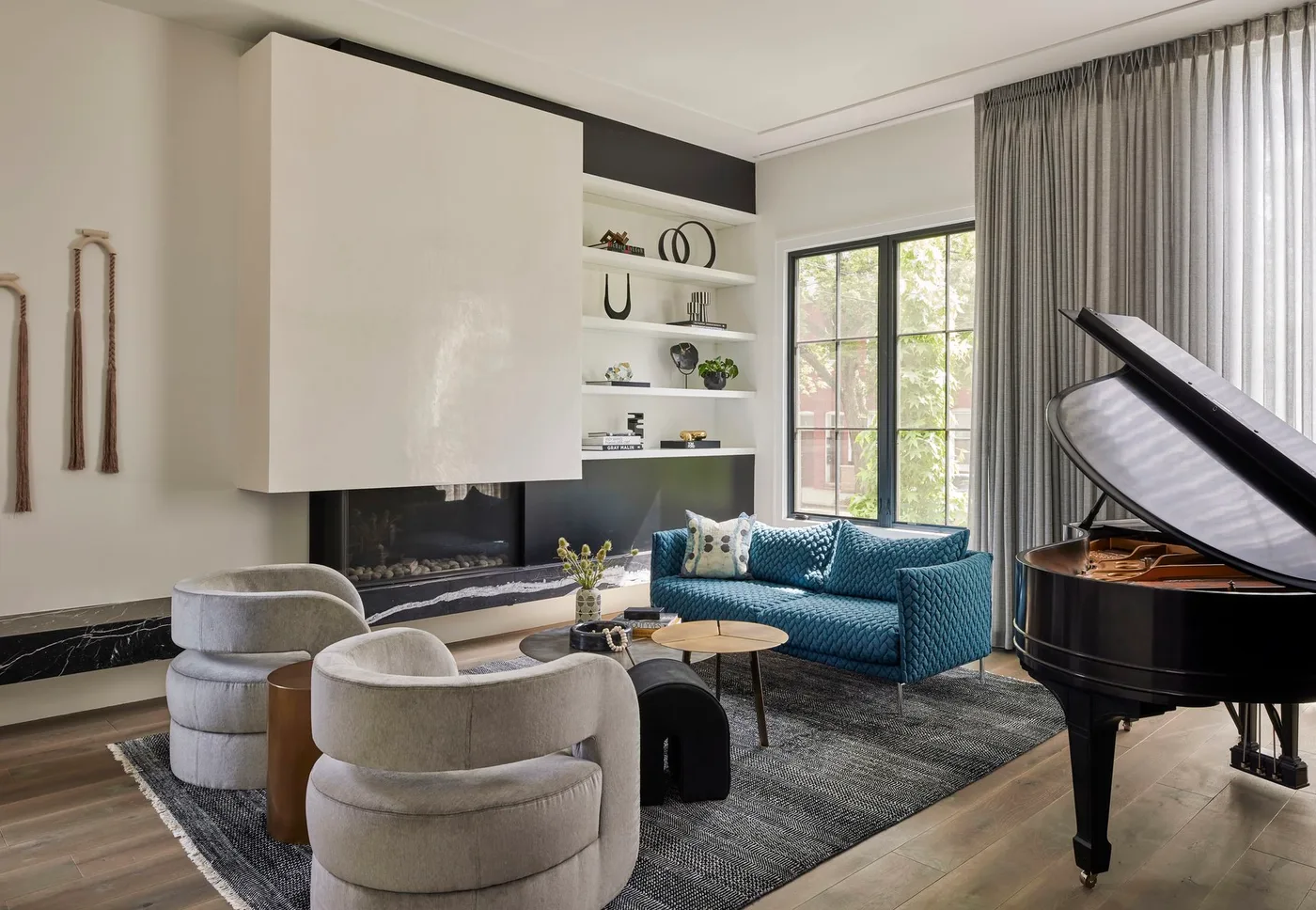 Modern white fireplace hood above long dark veined hearth in a room with gray chairs and piano