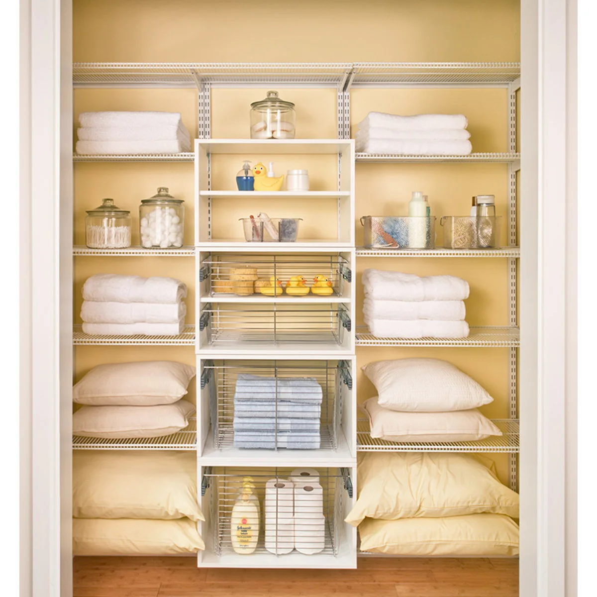 White linen closet with wire shelves, folded towels, pillows and a central column of pullout baskets