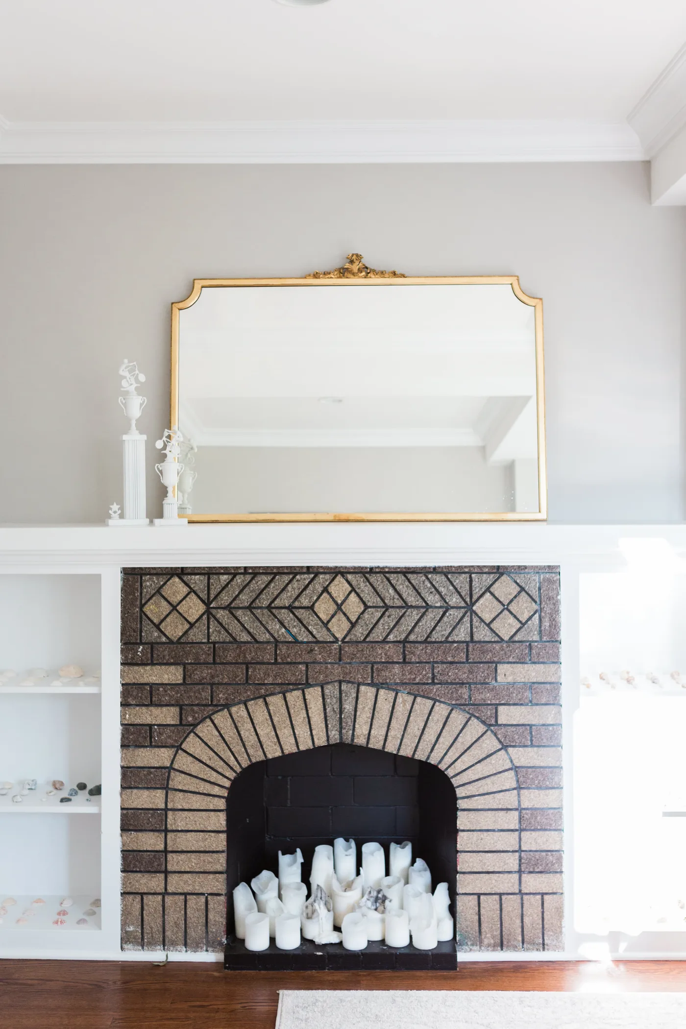 Patterned brick fireplace with dark opening containing pale pillars beneath a white mantel and large mirror.