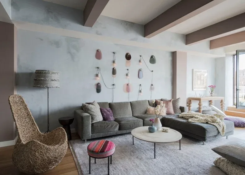 Gray sectional beneath a scattered wall display with a tall textured chair and pink round stool.