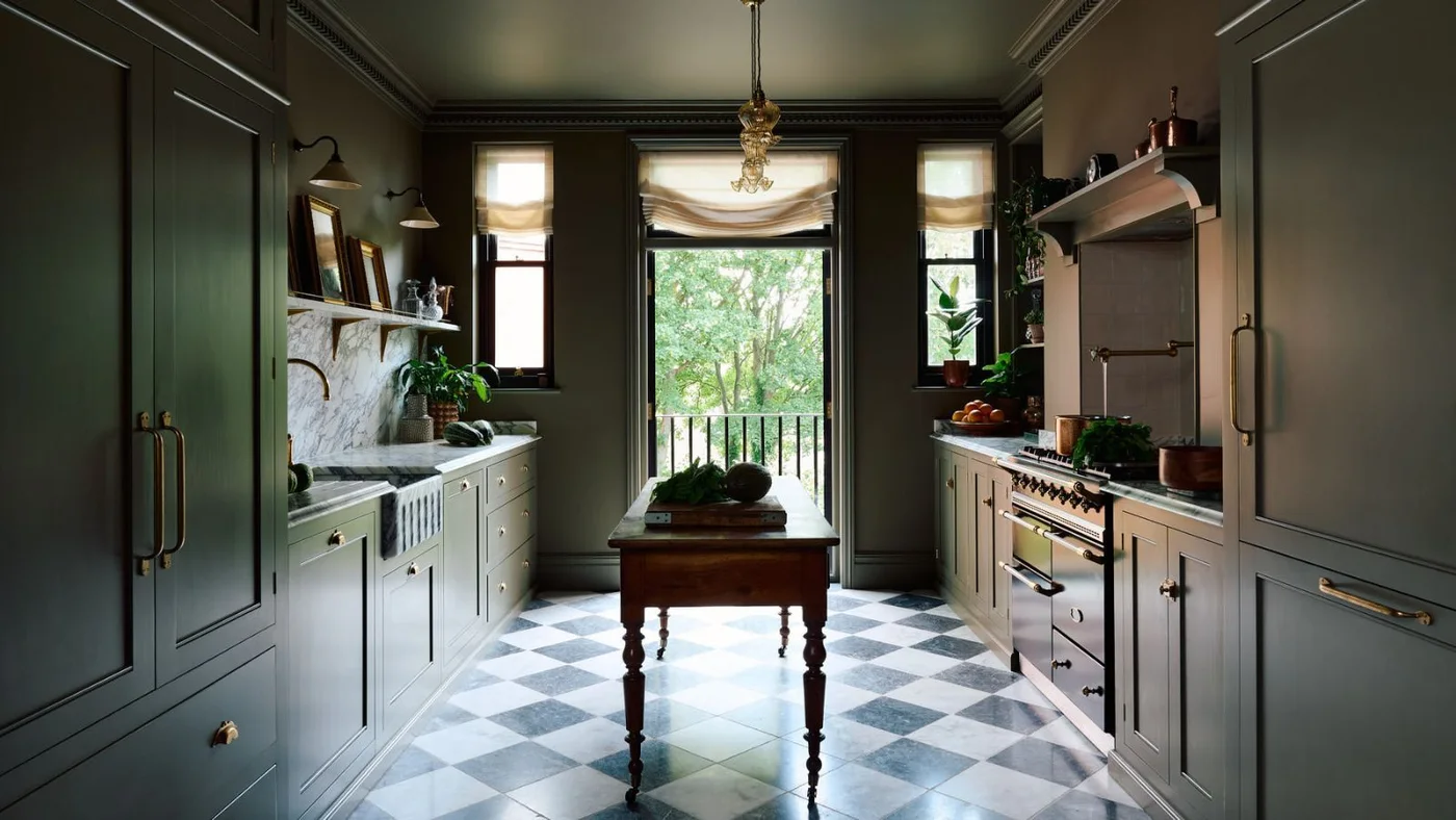 Green galley kitchen with a narrow wooden worktable on a checkerboard floor