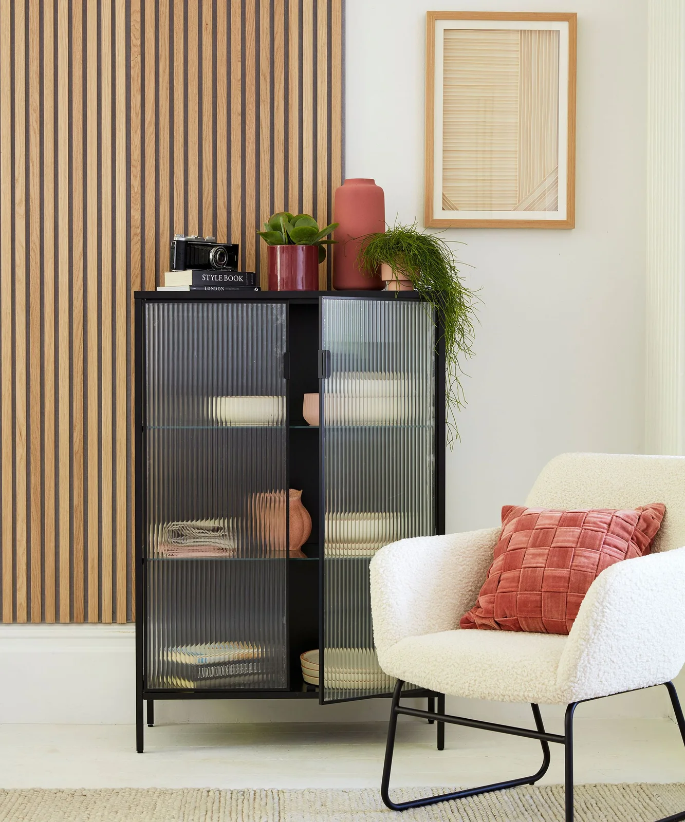 Black glazed cabinet with vertically textured doors holding bowls, books and small decorative pieces