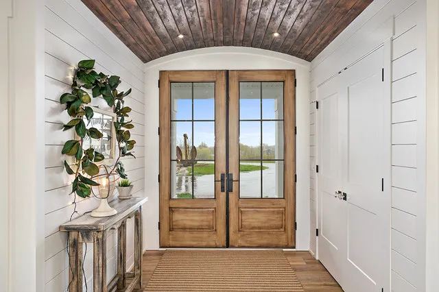 Timber double doors sit beneath a wood-lined ceiling between white paneled walls.