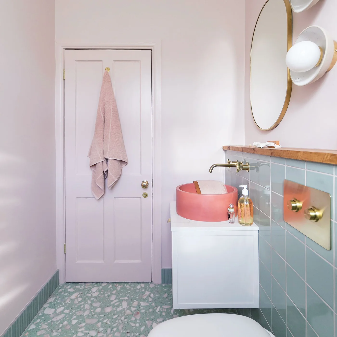 Pale pink walls and a pink-painted door meet green terrazzo flooring beside green tiles and a coral basin.