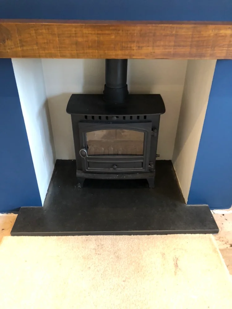 A dark stove sits inside a white recess in a blue chimney breast above a T-shaped slate hearth.