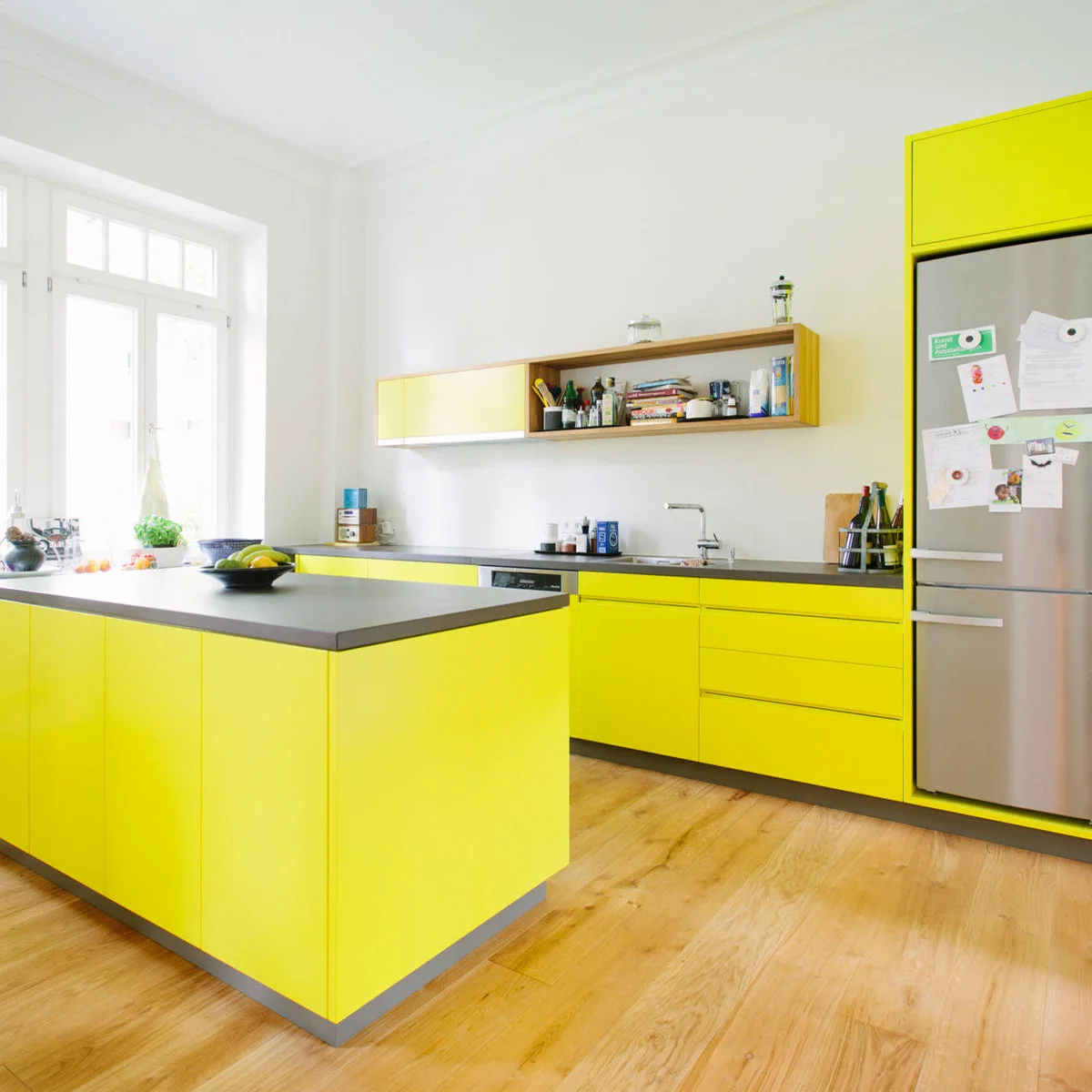 Lemon yellow flat-front kitchen cabinets with dark counters and open wood-colored shelving