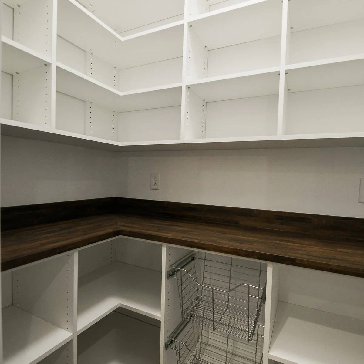 Empty white pantry with continuous corner shelves above a dark countertop