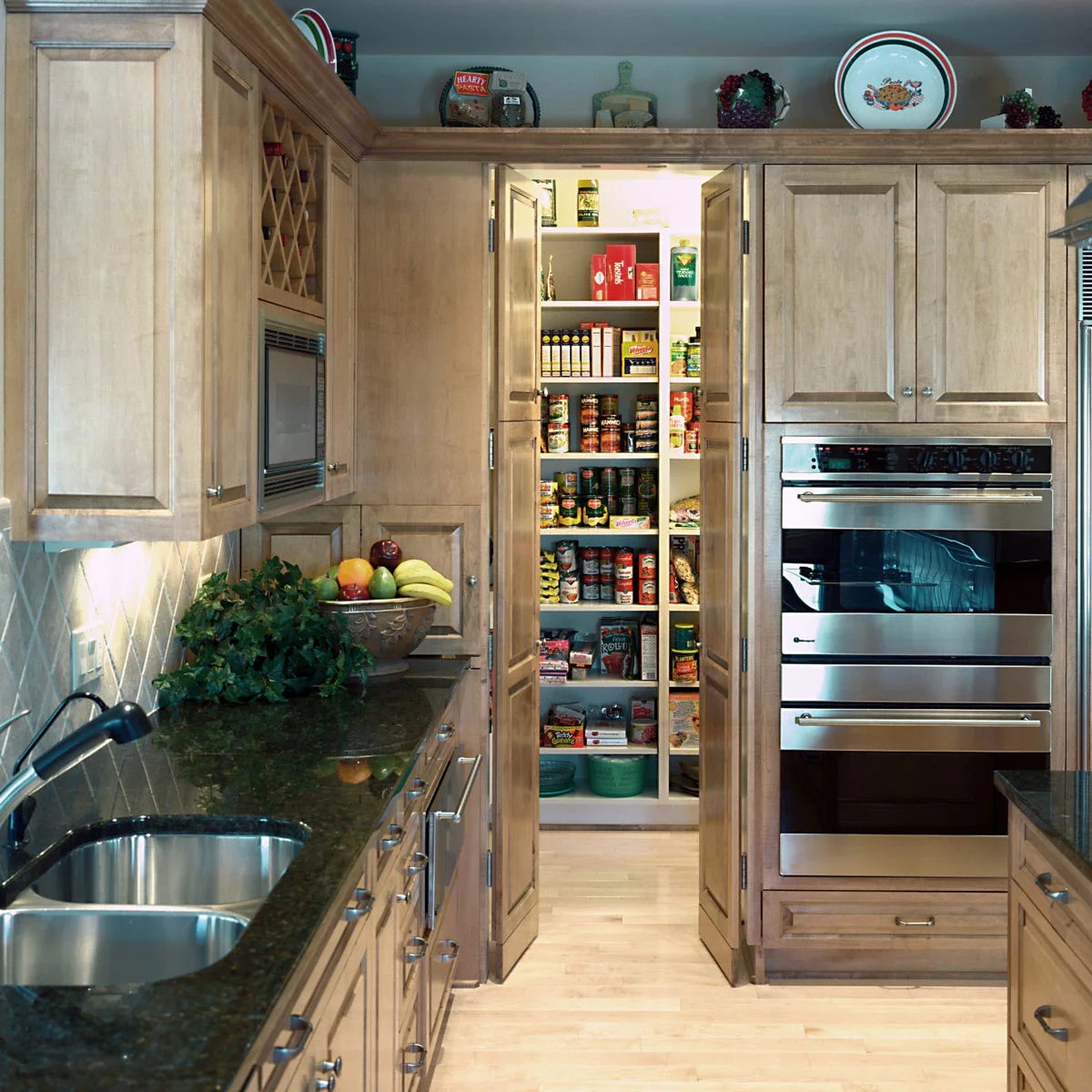 Paneled wood doors open onto narrow pantry shelves between a kitchen counter and a bank of ovens.