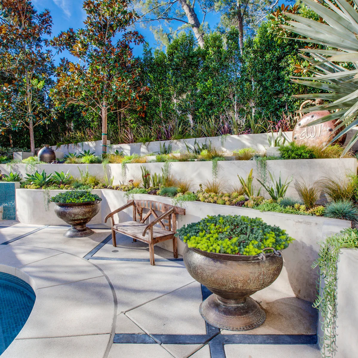 Pale concrete retaining walls create three planted levels above a poolside patio.