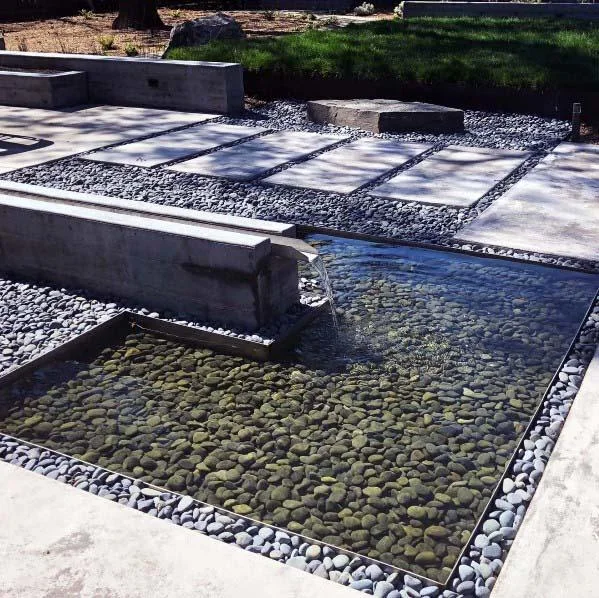 Dark rounded stones fill the bottom of a rectangular water feature and the strips between adjacent pavers