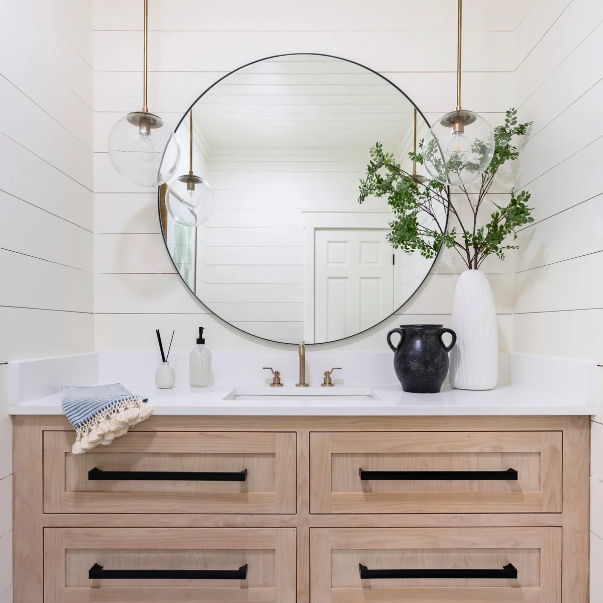 Large black-rimmed round mirror above a wooden vanity with hanging glass lights