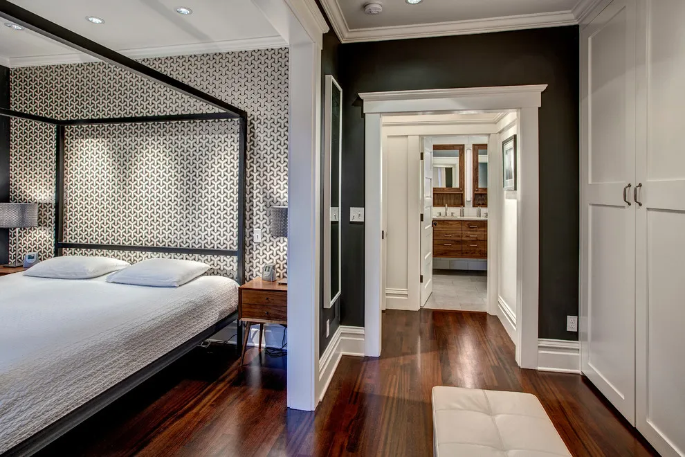 Dark bedroom with a slim four-poster bed, white fitted wardrobe and a clear passage to a bathroom