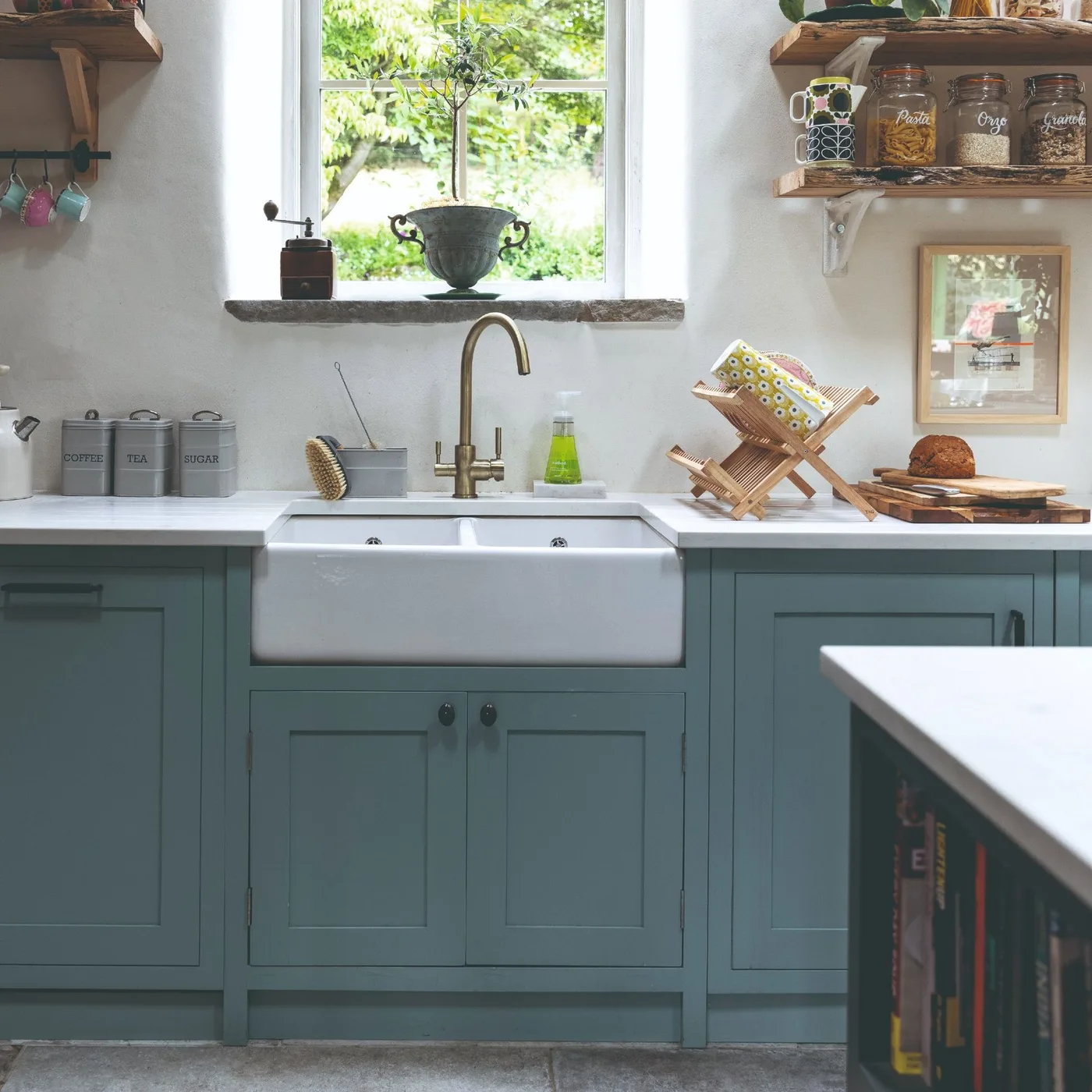 Kitchen sink area with blue-green framed cabinets, a white apron-front sink, gold-colored tap and open wooden shelves.