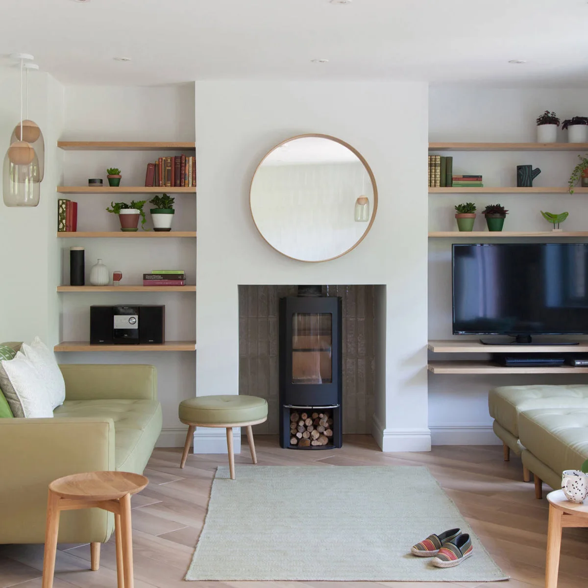 Wood shelves with small plants, books and a teal jug above a television in an alcove beside a white fireplace wall.