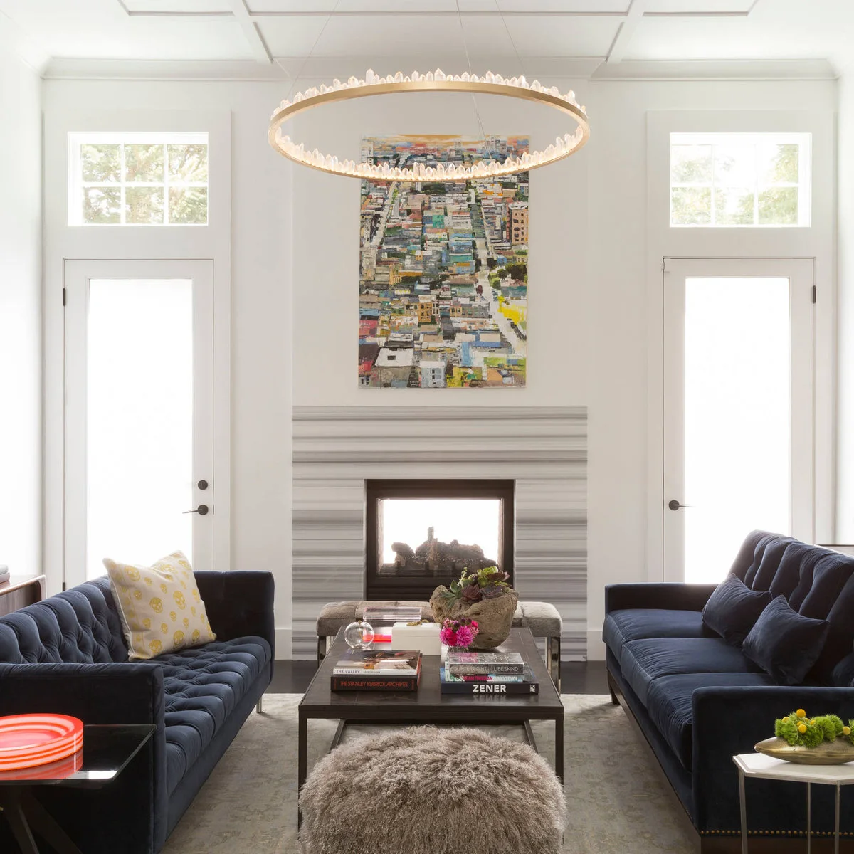 Two navy sofas face each other across a dark rectangular table in a white room with doors beside the fireplace.
