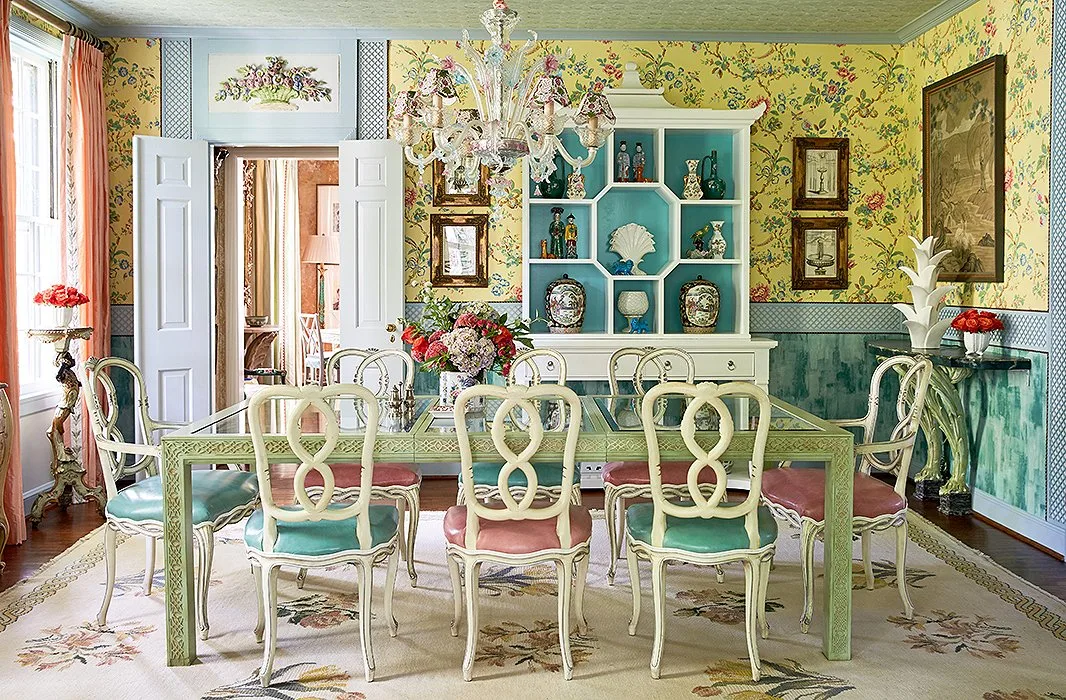 Floral yellow wallpaper around a pale green dining table, light curved chairs and a decorative display cabinet.