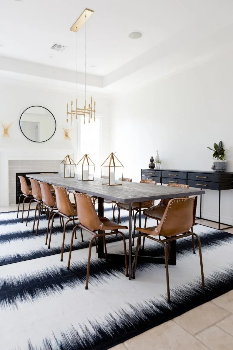 Three gold-framed glass lanterns with pale candles on a long gray dining table surrounded by brown chairs