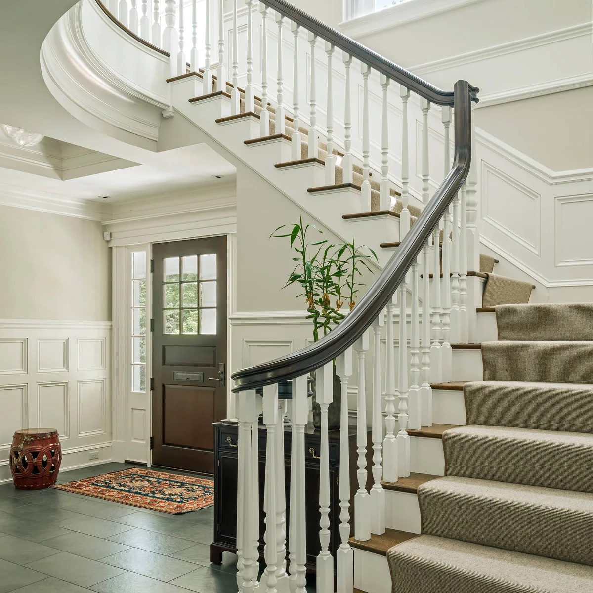 Traditional white staircase with a plain beige runner, dark curved handrail and paneled walls