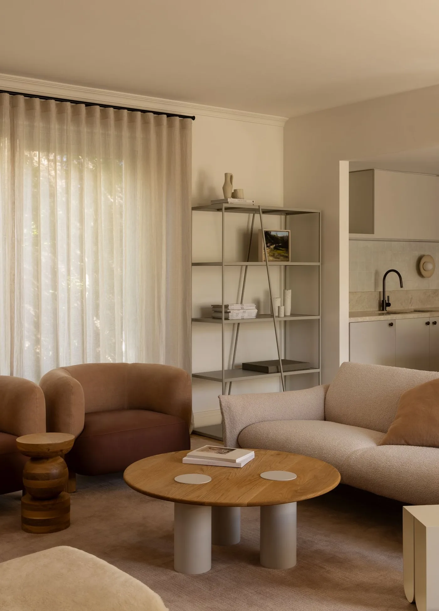 Rounded brown chairs with a pale sofa, wood-topped round coffee table and lightly filled open shelving