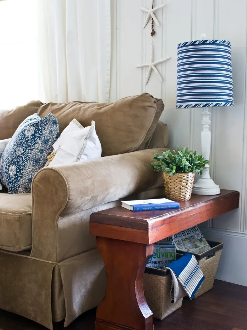Tan sofa beside a narrow wooden bench-style table with a blue striped lamp and small woven plant basket.