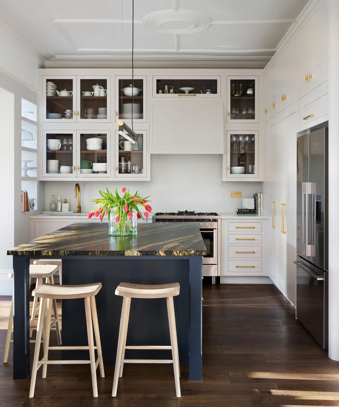 Off-white cabinets with glass upper doors and warm metal handles surround a dark blue island with a strongly patterned counter.