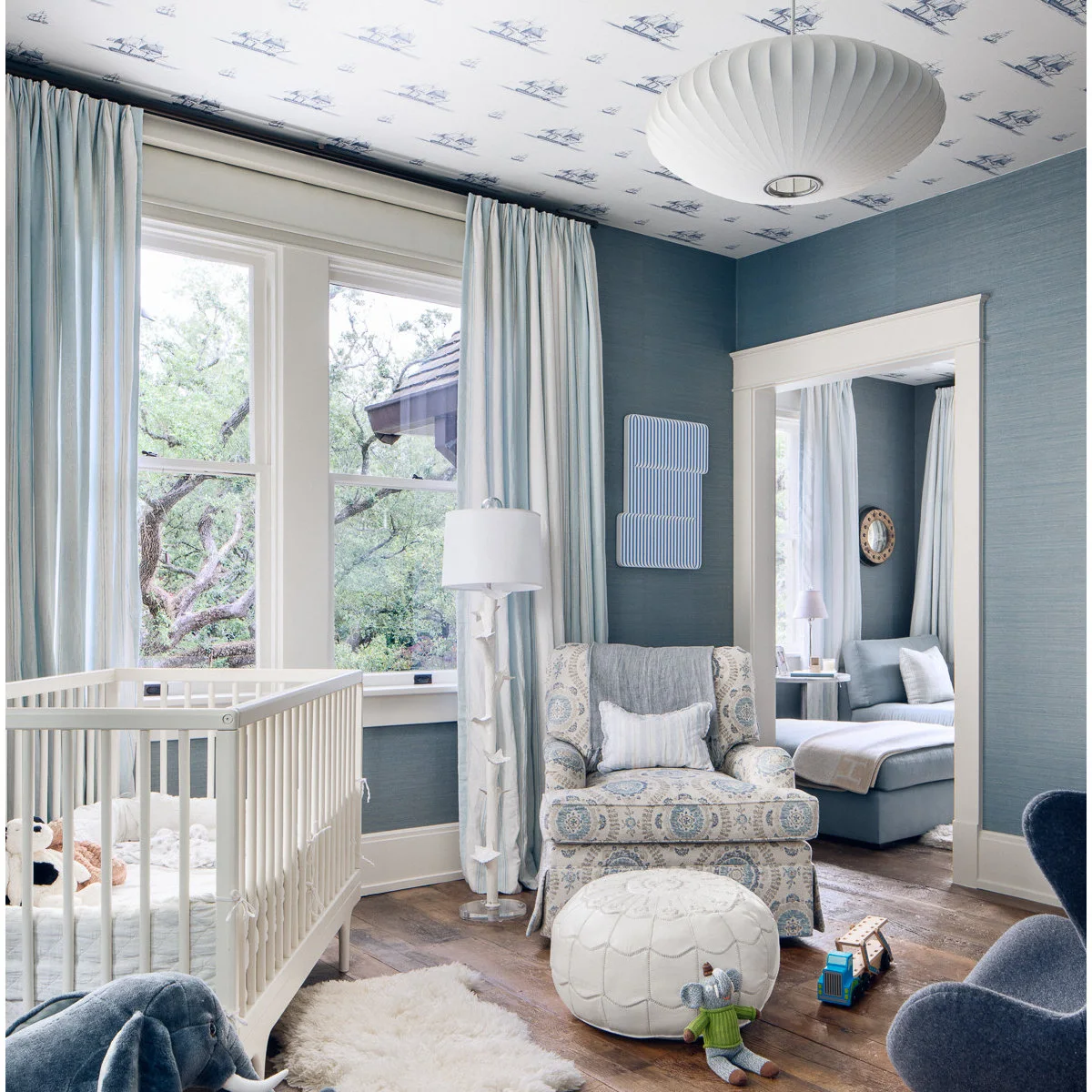 Nursery with a ship-pattern ceiling, blue walls, pale crib and upholstered adult chair