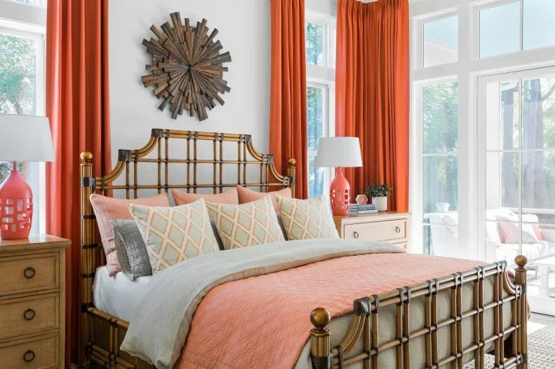 White bedroom with coral curtains and bedding, an open warm-toned bed frame, wooden bedside drawers and a round wooden wall decoration.