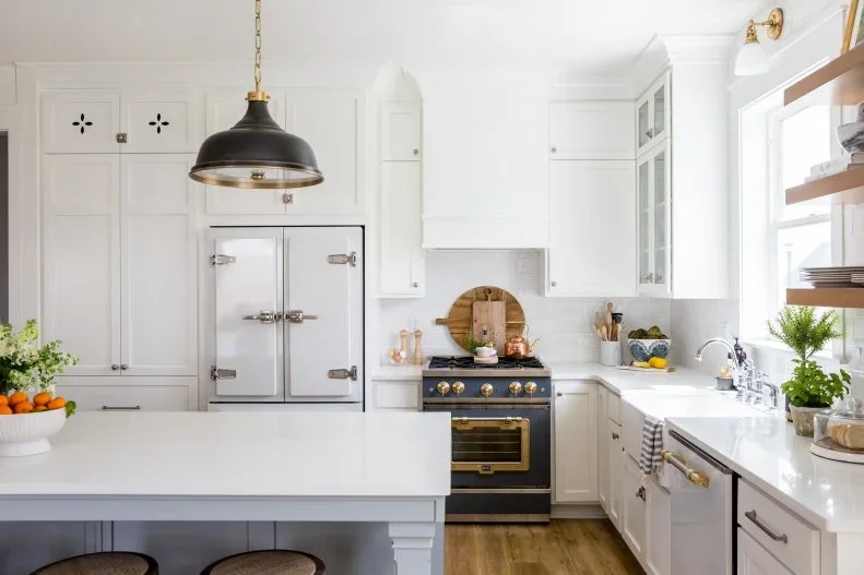 White framed cabinets and pale counters surround a blue range beneath a dark dome pendant and a white hood.
