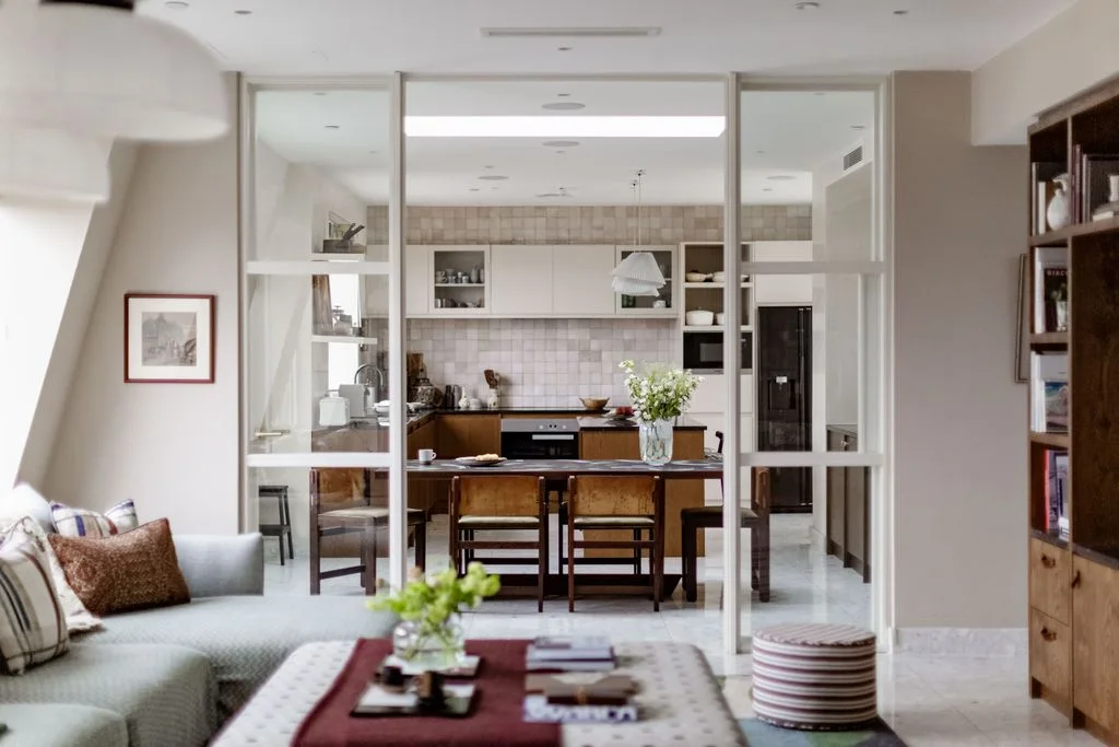 A pale sofa faces an open glazed partition leading to a kitchen and timber dining table.