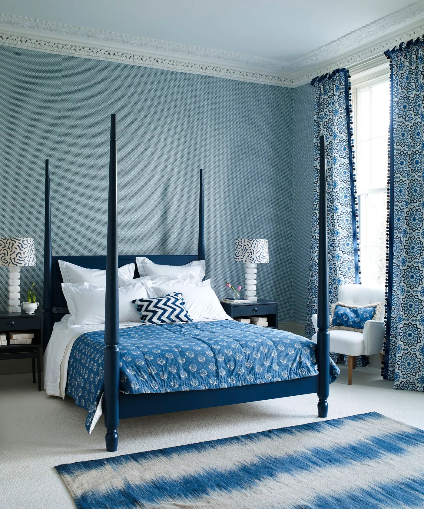 Dark blue four-poster bed in a blue patterned room with white bedding and floral blue textiles.