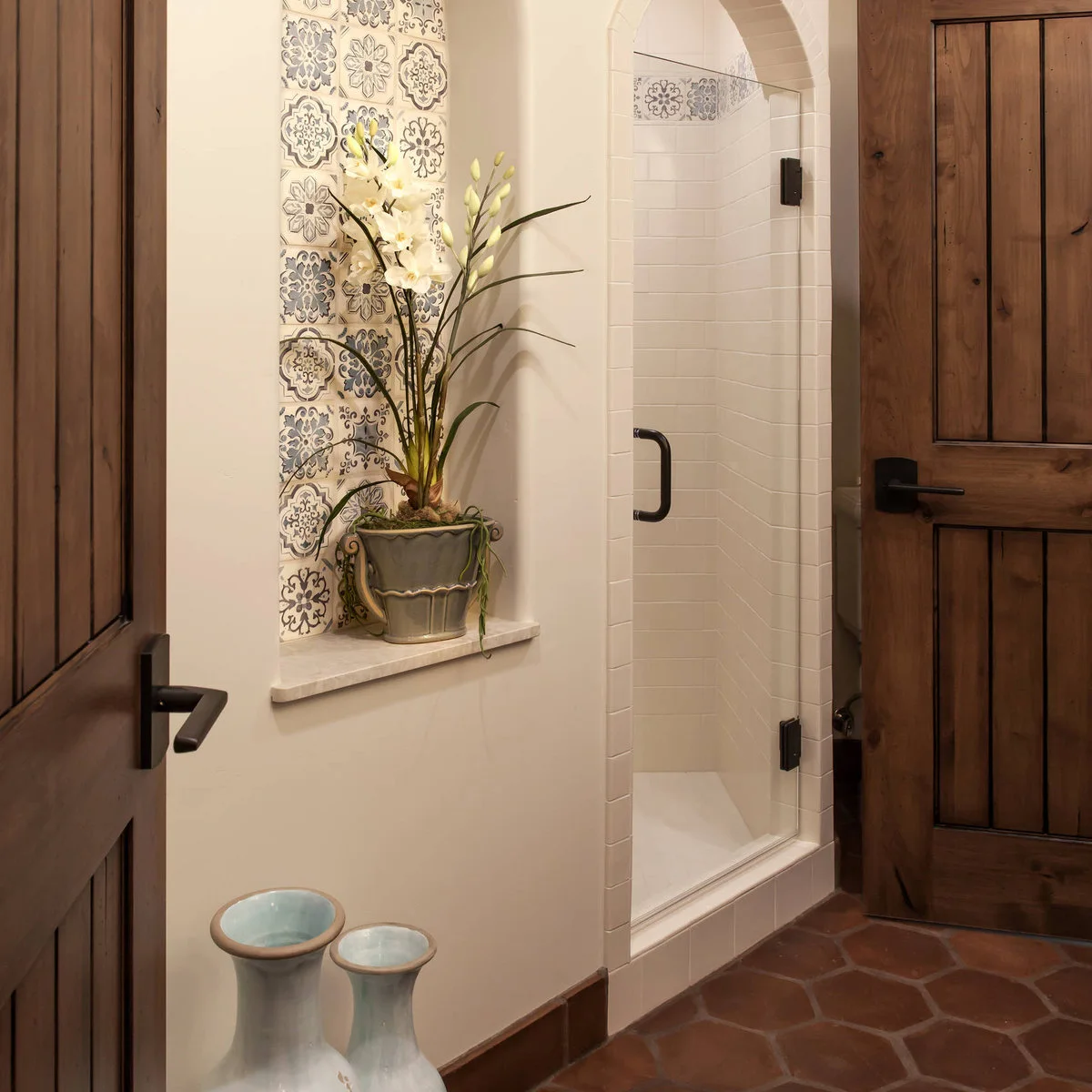 Bathroom with a narrow patterned tile recess, white arched shower and terracotta-colored hexagonal floor