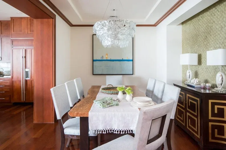 Wooden dining table with white chairs, a clear bubble chandelier and a dark sideboard outlined in gold-toned geometric lines.