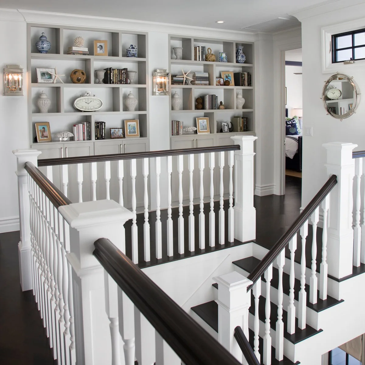 White staircase landing with dark handrails opposite built-in bookshelves and closed lower cupboards