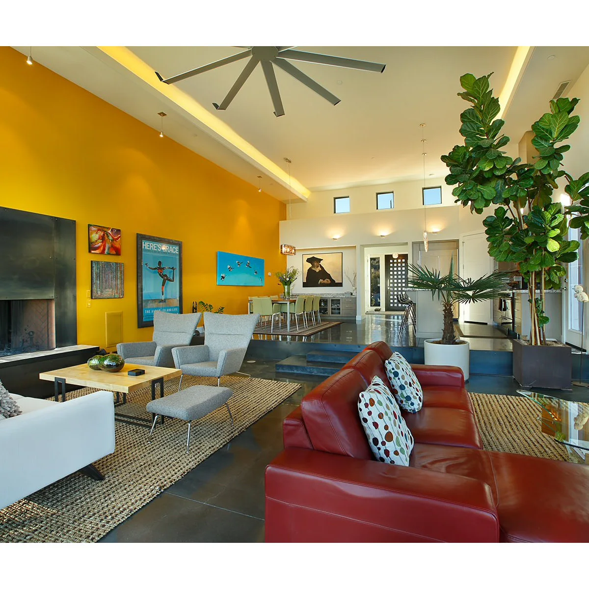 Light gray chairs and footstool sit beside a reddish brown sofa beneath a tall golden yellow wall.