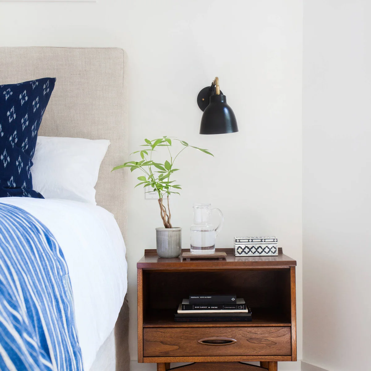 Wooden nightstand with one drawer and open shelf beneath a black wall light