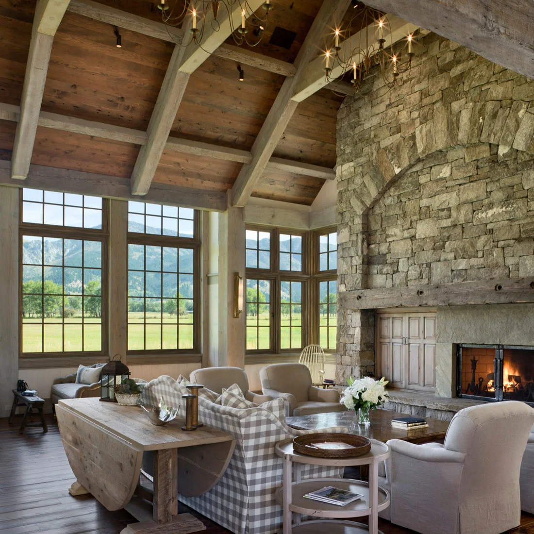 A timber drop-leaf table holds a lantern and small objects behind a checked sofa near a stone fireplace.