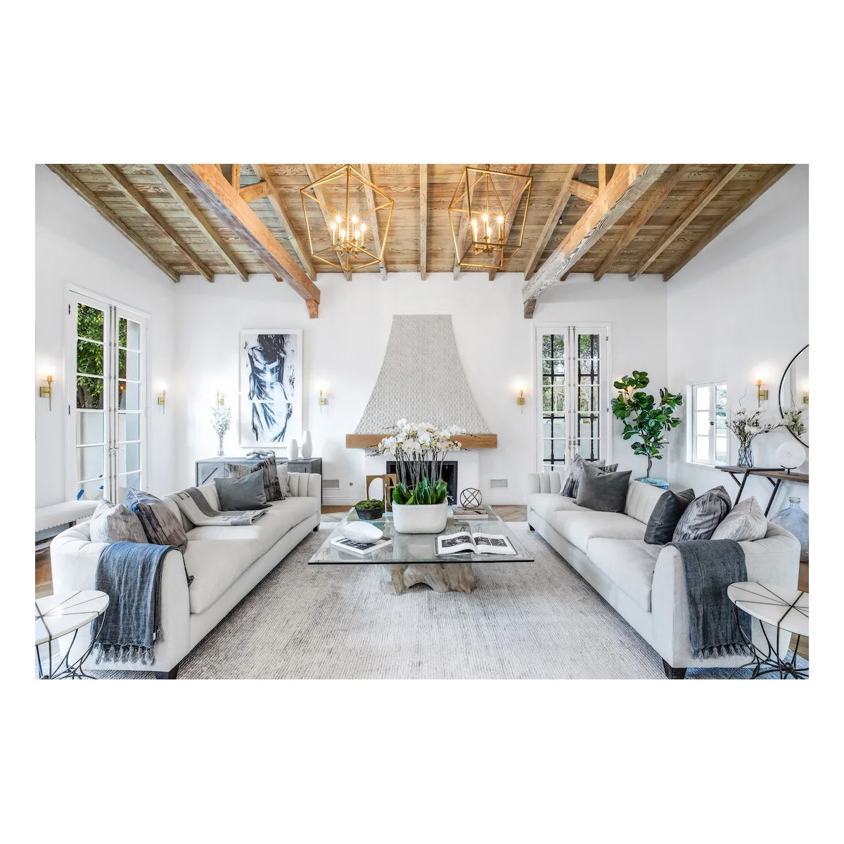 Exposed-beam living room with opposing pale sofas, two open lantern pendants and a fireplace at the far end