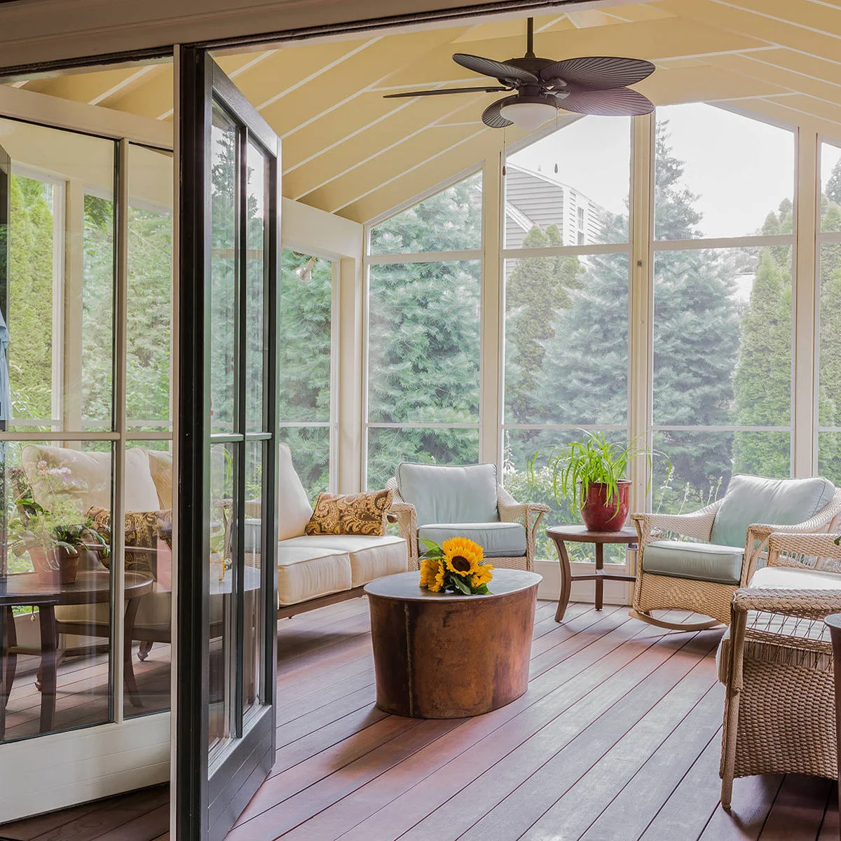 A pale yellow vaulted porch ceiling above wicker chairs, light cushions and a small round central table.