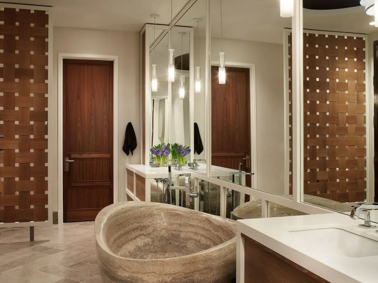 A banded brown stone tub sits beside pale counters, mirrors and a timber woven-look room divider.