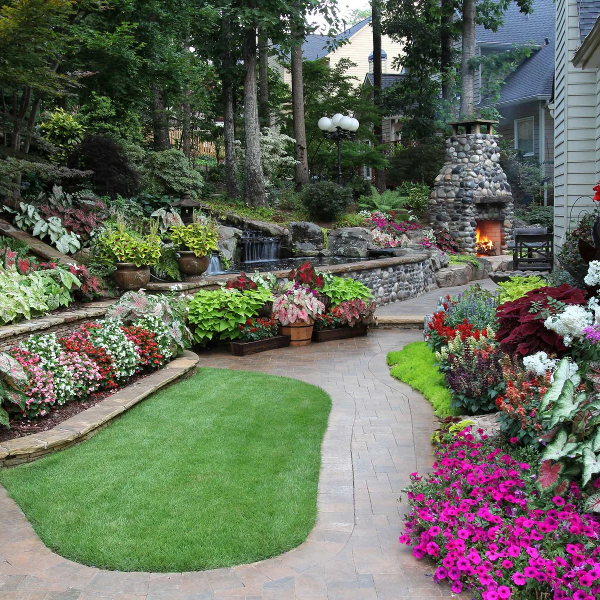 A low stone-faced flower bed with flat coping curves beside a lawn and paved garden path.