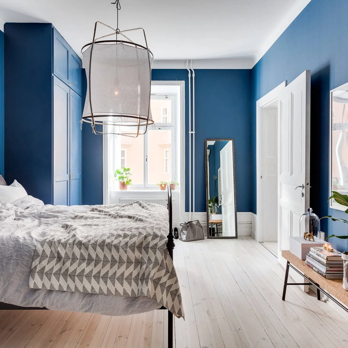 Mid-blue bedroom walls and matching tall cabinets with white floorboards and gray patterned bedding.