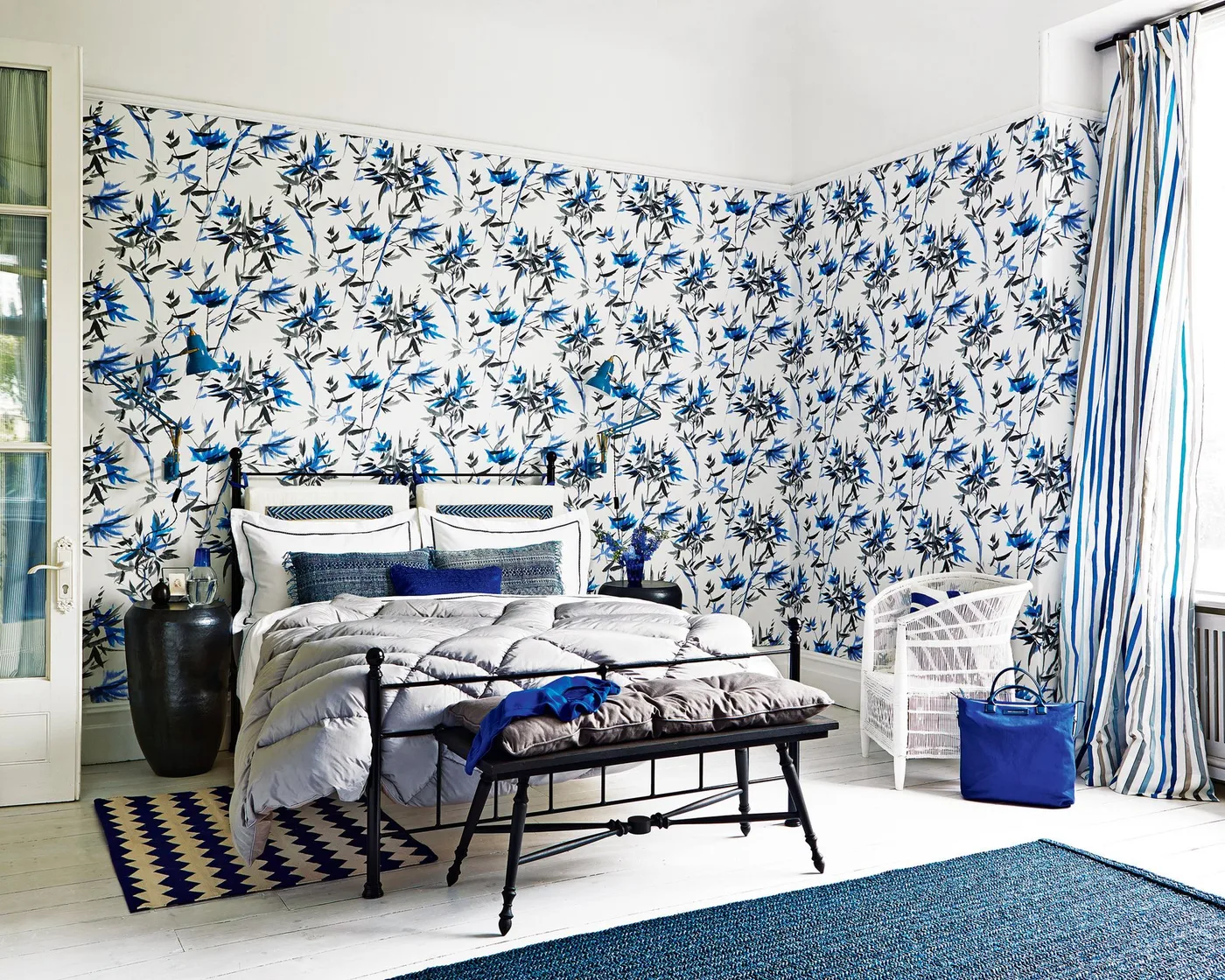 Black metal bed and bench in a room with blue botanical wallpaper and blue-and-white curtains.