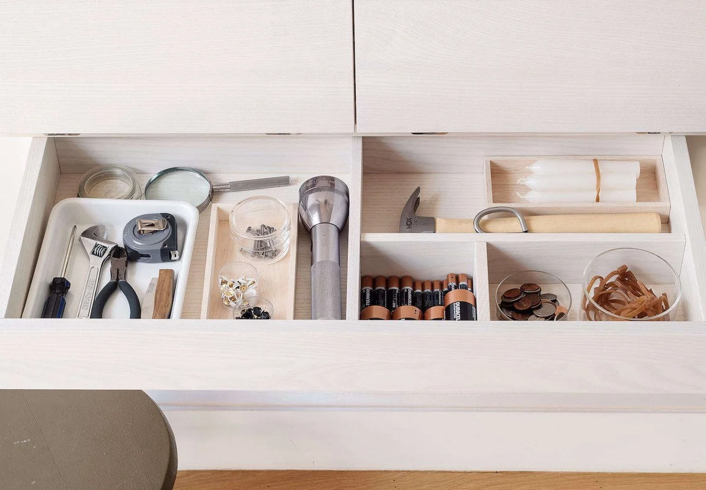 Pale wooden utility drawer with a hammer, flashlight, pliers, tape measure and small separated supplies