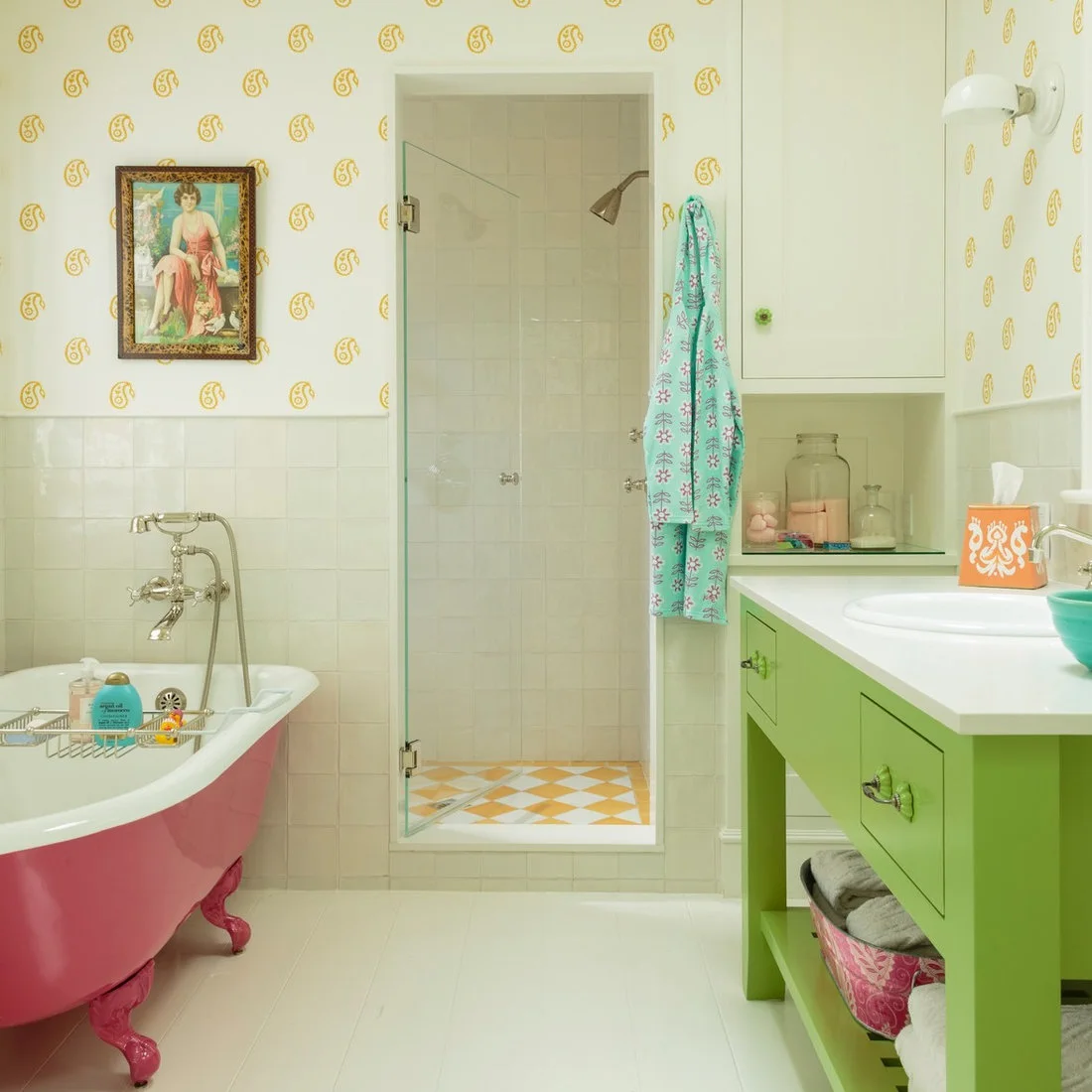 A pink claw-foot tub faces a bright green vanity beside pale walls and a glass shower enclosure.
