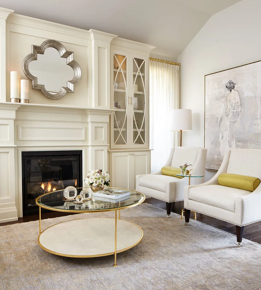 Two pale high-backed chairs with yellow cushions sit near a white fireplace and round glass table